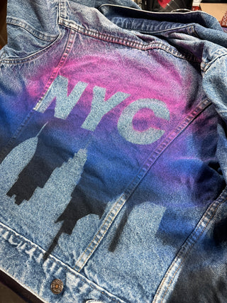 Hand-painted custom jean jacket by Sara Joy. Painted with pinks and purples, and featuring the New York skyline and 'NYC' letters.