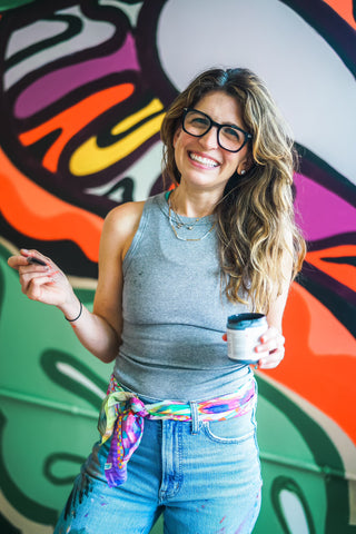 A close-up of NYC Mural Artist, Sara Joy. Sara is posing in front of her large, brightly colored mural at The Lark in New York.